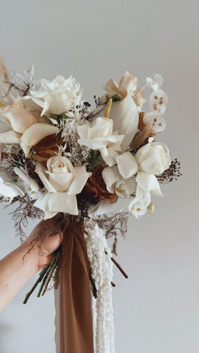 a person holding a bouquet of flowers in their hand and wearing a brown ribbon around it