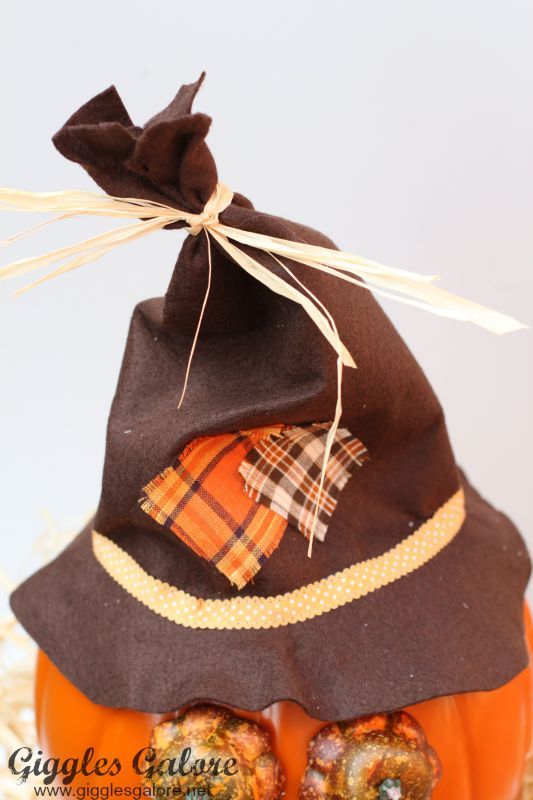 an orange pumpkin with a black hat and plaid fabric on it's top, sitting in hay