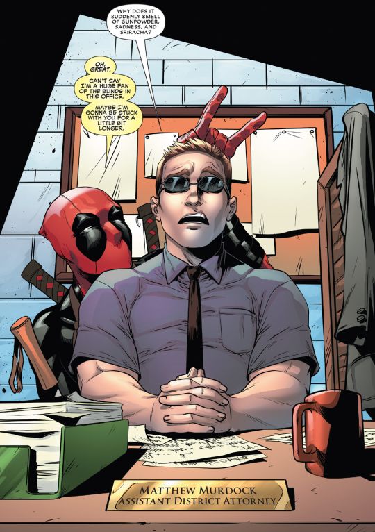 a man sitting at a desk with a deadpool on his head and glasses in front of him