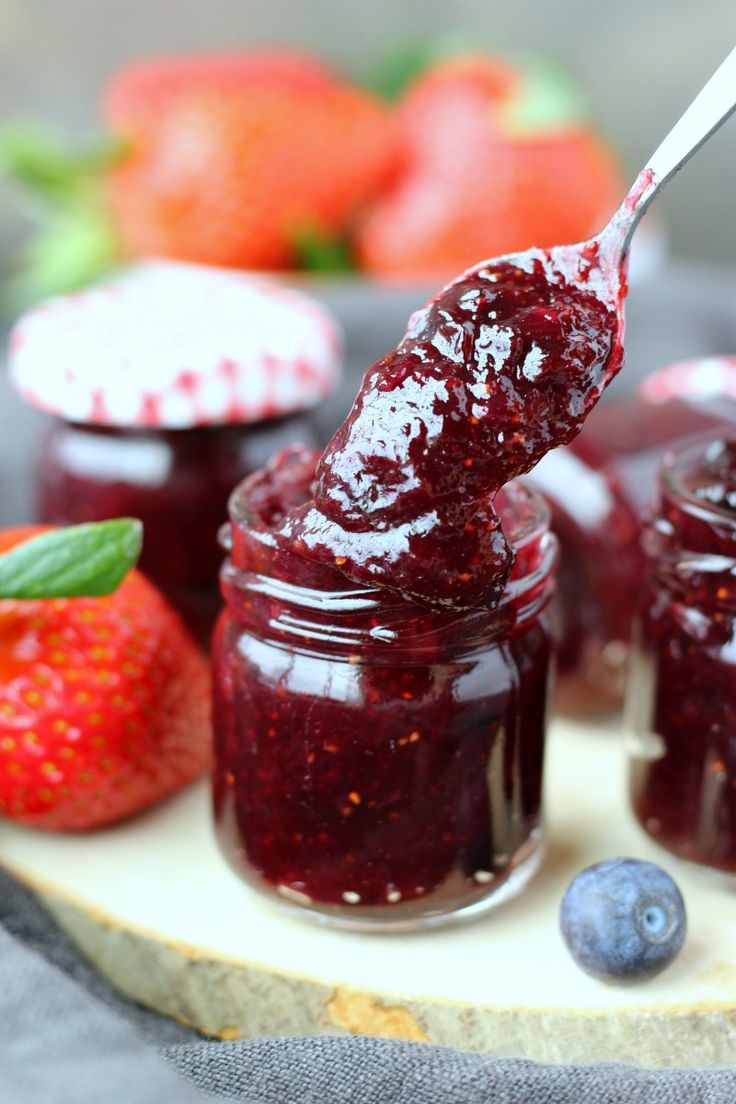 a spoon full of jam on top of a cutting board with strawberries and blueberries in the background