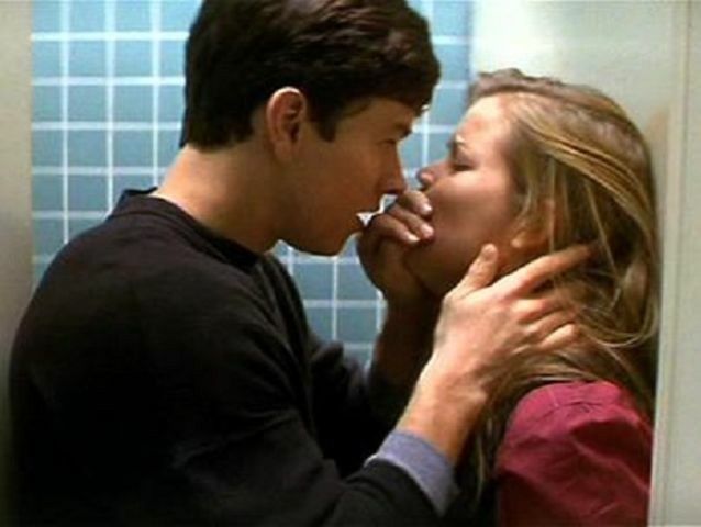 a man and woman kissing in front of a bathroom mirror with blue tiles on the wall