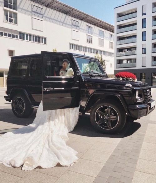 the bride and groom are sitting in their black mercedes g class wedding car, which is decorated with red flowers