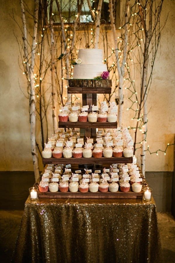 a wedding cake and cupcakes on a table in front of some trees with lights