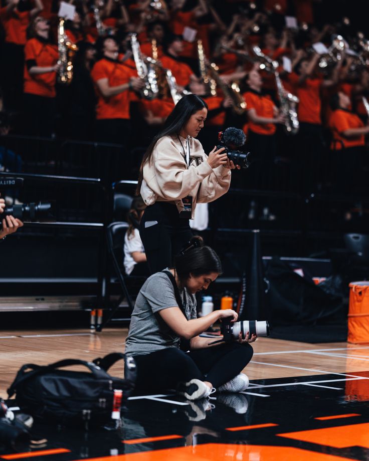 a woman sitting on the floor with a camera in front of her and people behind her