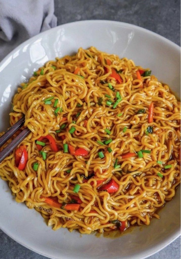 a white bowl filled with noodles and vegetables next to chopsticks on a table