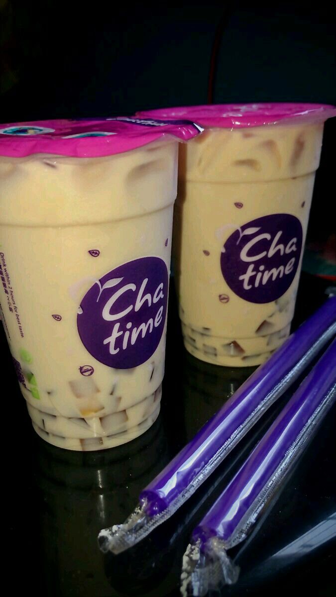 two ice cream cups with purple straws next to each other on a black table