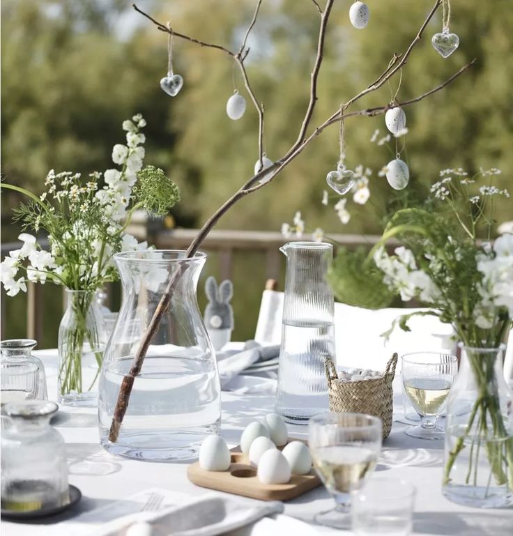 the table is set with vases, glasses and flowers on it for an easter brunch