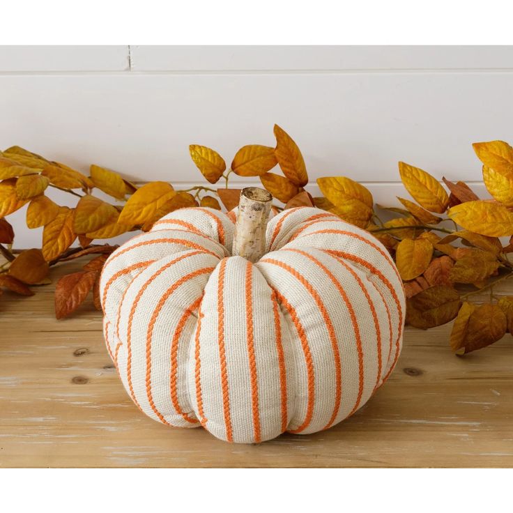 an orange and white striped pumpkin sitting on top of a wooden table next to leaves