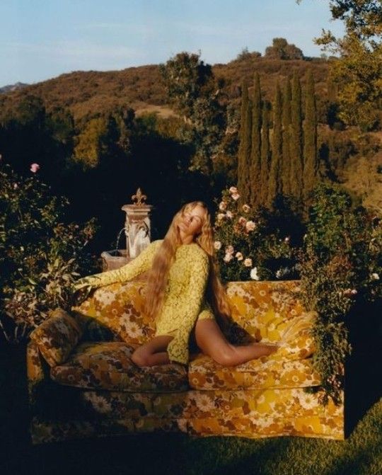 a woman sitting on top of a bed covered in yellow and pink flowers next to a lush green hillside