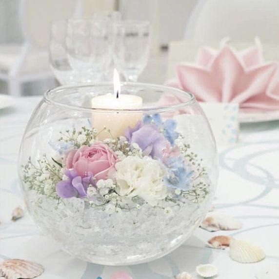 there is a candle that is in the bowl with flowers on it and seashells around it