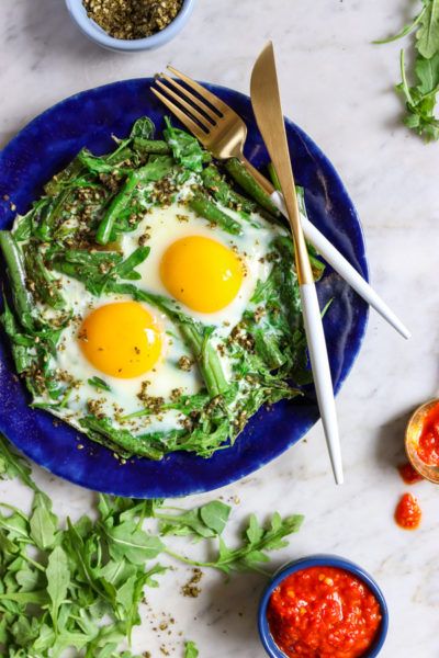 two fried eggs on top of lettuce in a blue plate with silverware