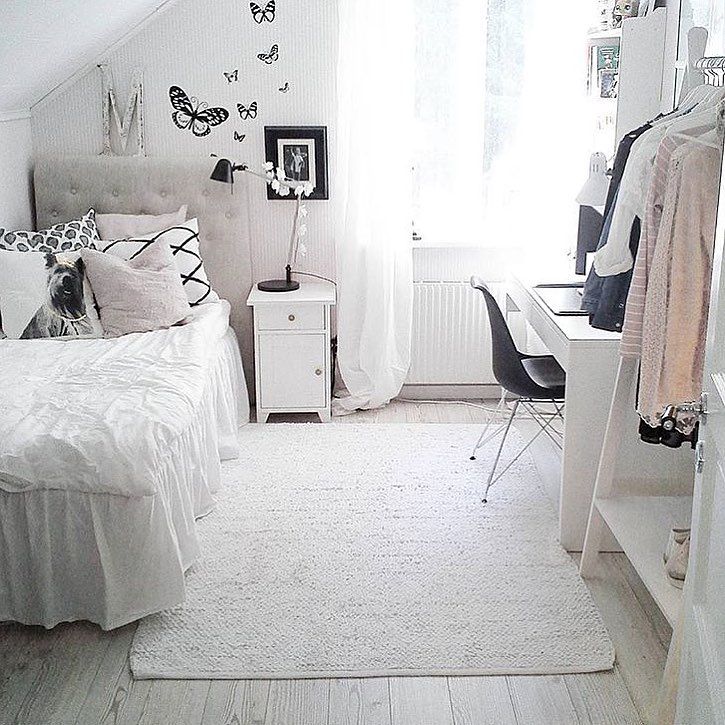 a bedroom with white walls and flooring has a bed, desk, chair, mirror and closet