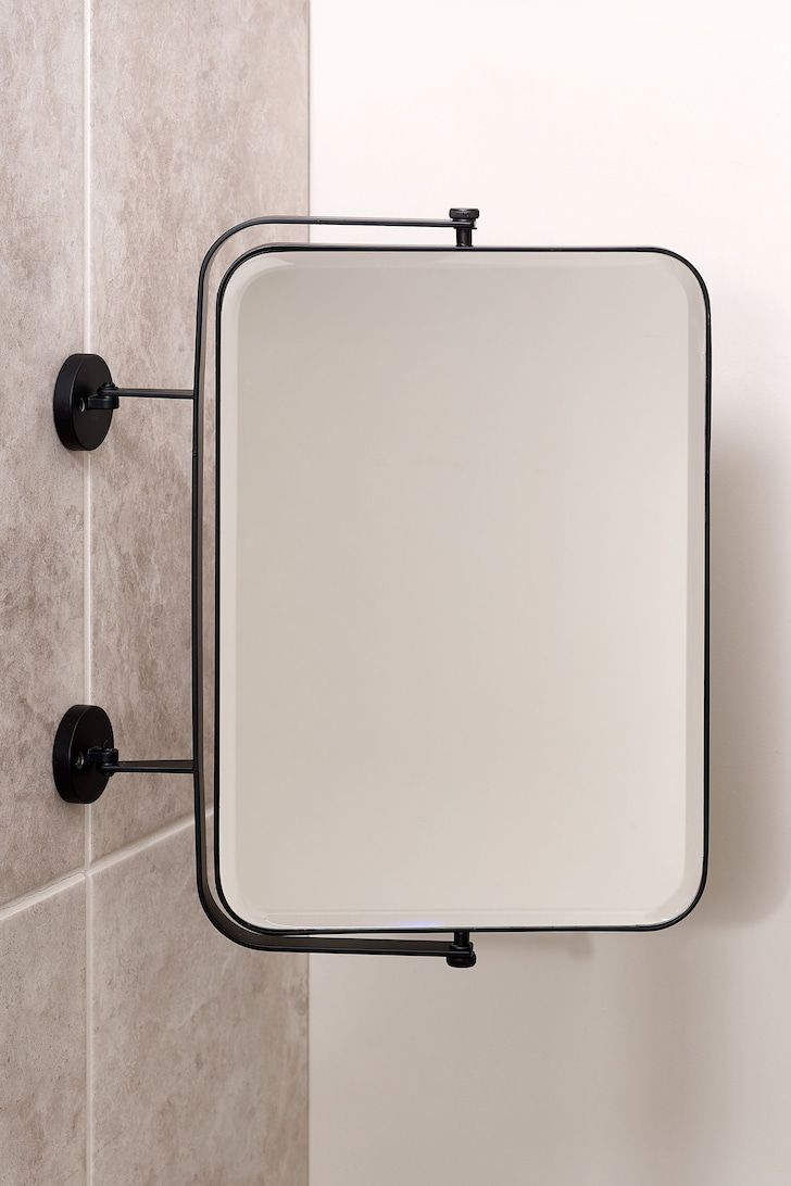 a bathroom mirror mounted on the wall next to a tiled shower stall with black fittings