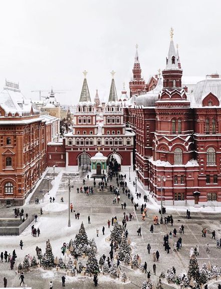 many people are walking around in the snow near some buildings with towers and spires