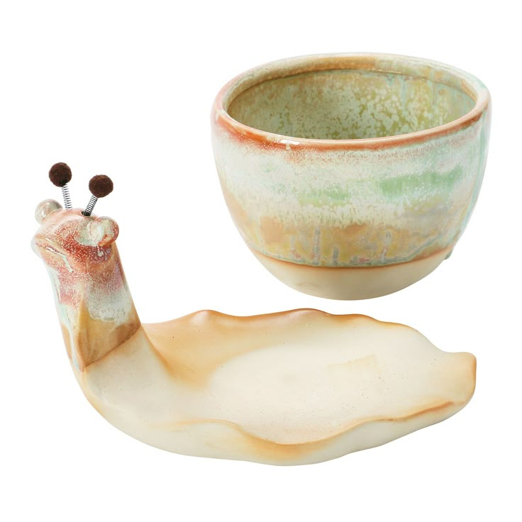 a ceramic bowl with a snail on the side next to it's lid and spoon