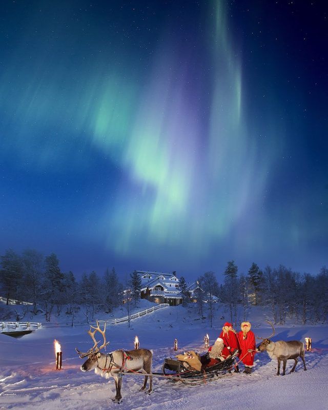 two reindeers pulling sleigh with people in the snow under an aurora bore