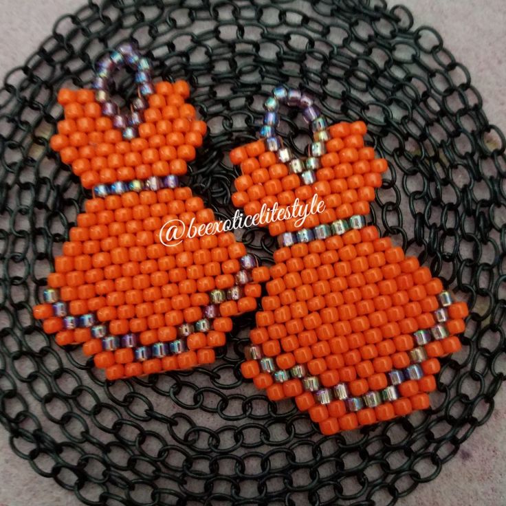 two orange birds are sitting on a black mesh tray with silver beads and chains attached to them