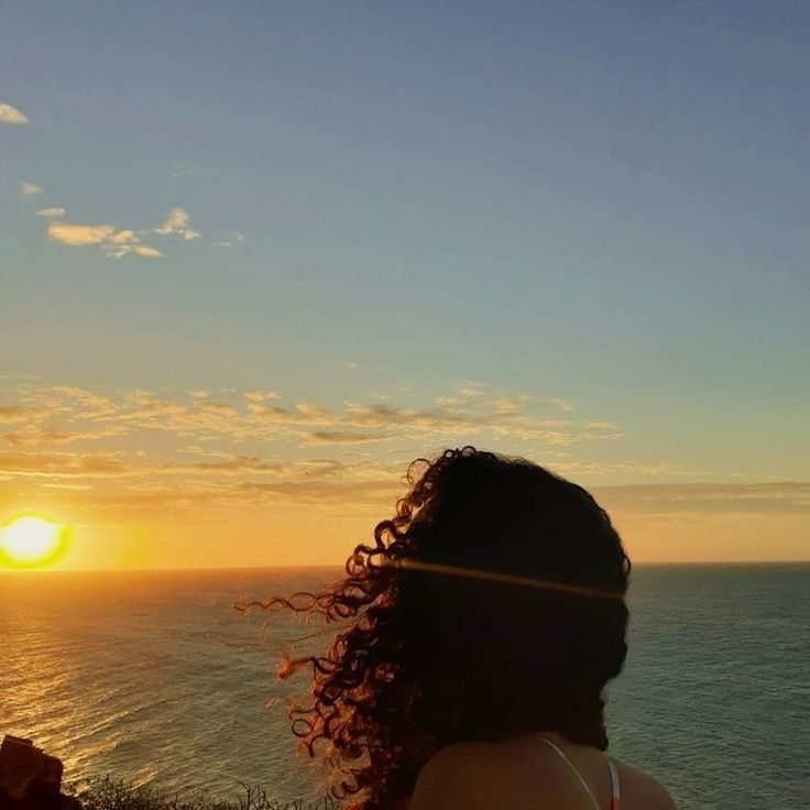 a woman looking out over the ocean at sunset