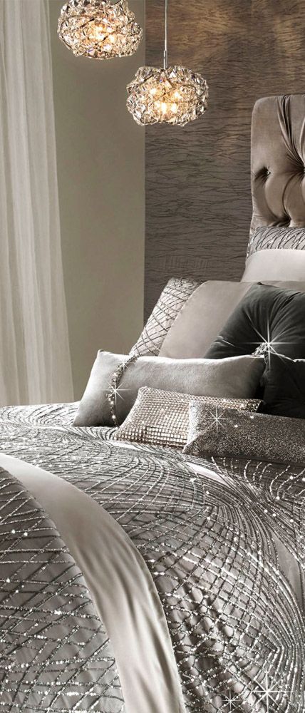 a bed with silver sheets and pillows in a bedroom next to two lights hanging from the ceiling