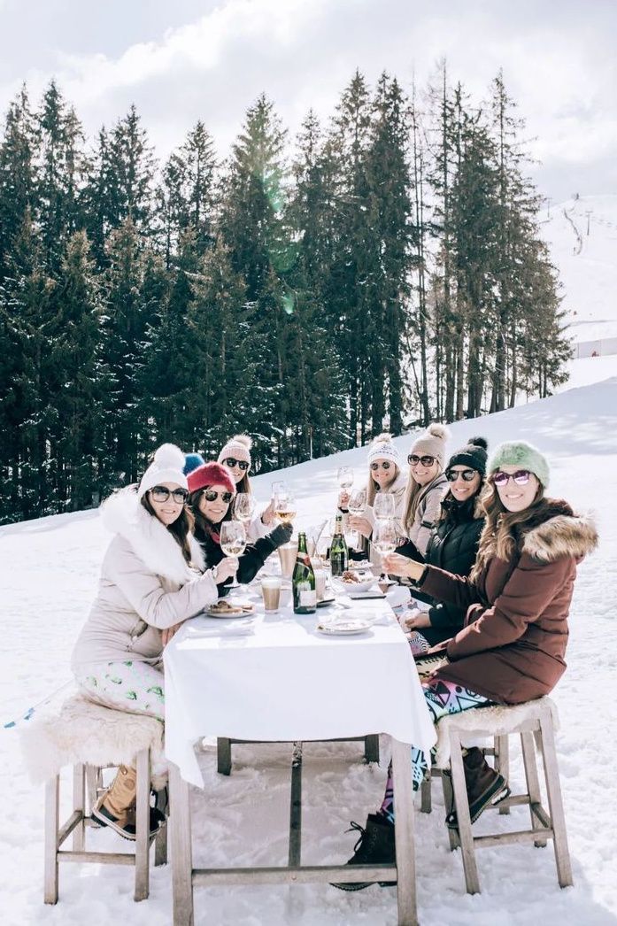 a group of people sitting at a table in the snow with wine bottles and glasses