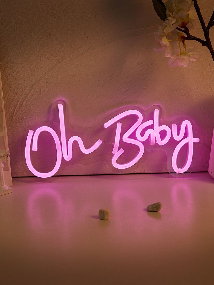 a pink neon sign that says oh baby on the side of a wall next to a vase with flowers