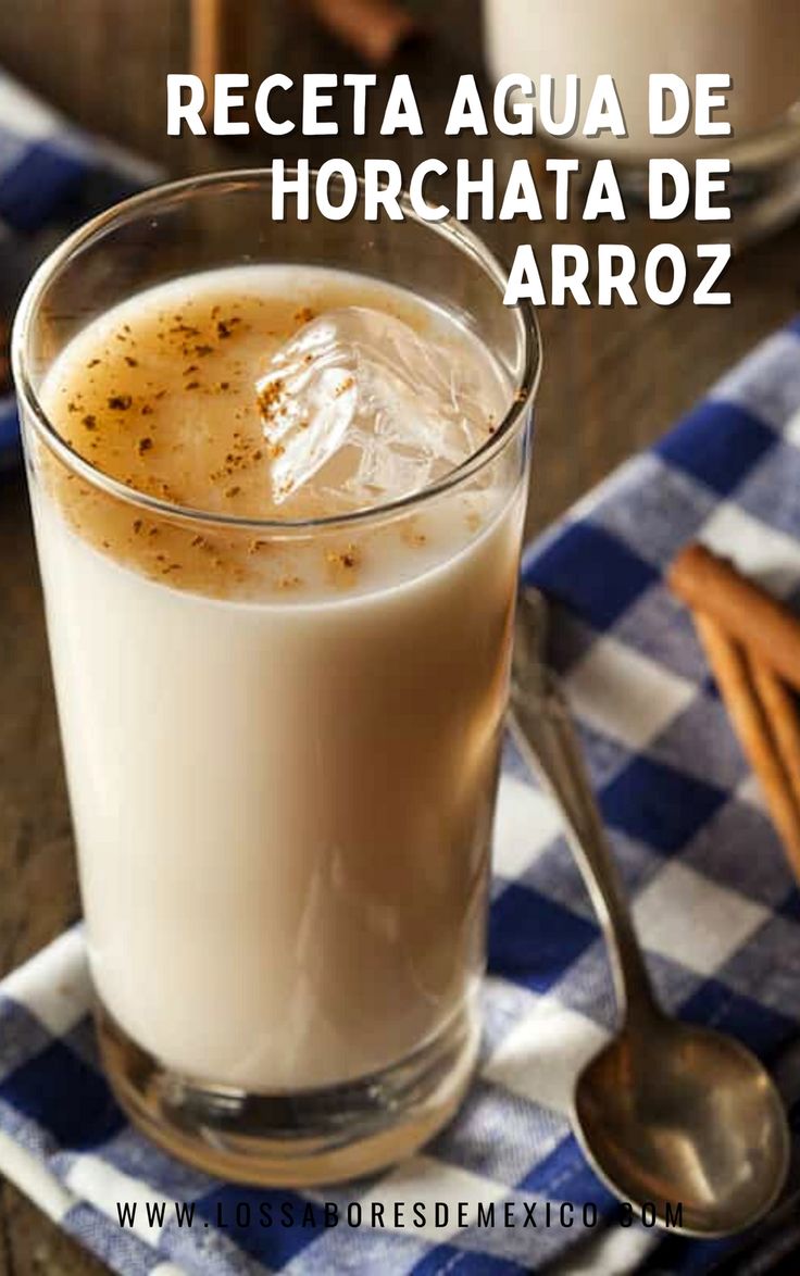 a glass filled with liquid sitting on top of a wooden table next to spoons