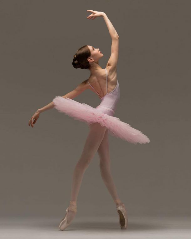 a ballerina in a pink tutu and leotard with her arms stretched out