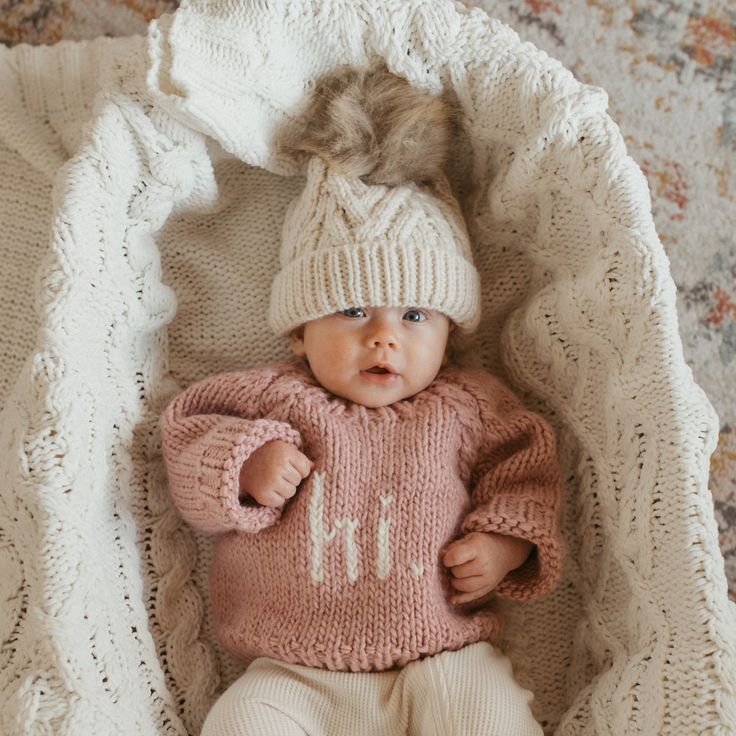 a baby wearing a knitted sweater and hat laying in a blanket on the floor