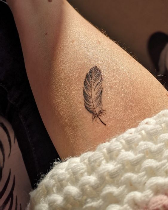 a woman's arm with a small feather tattoo on it