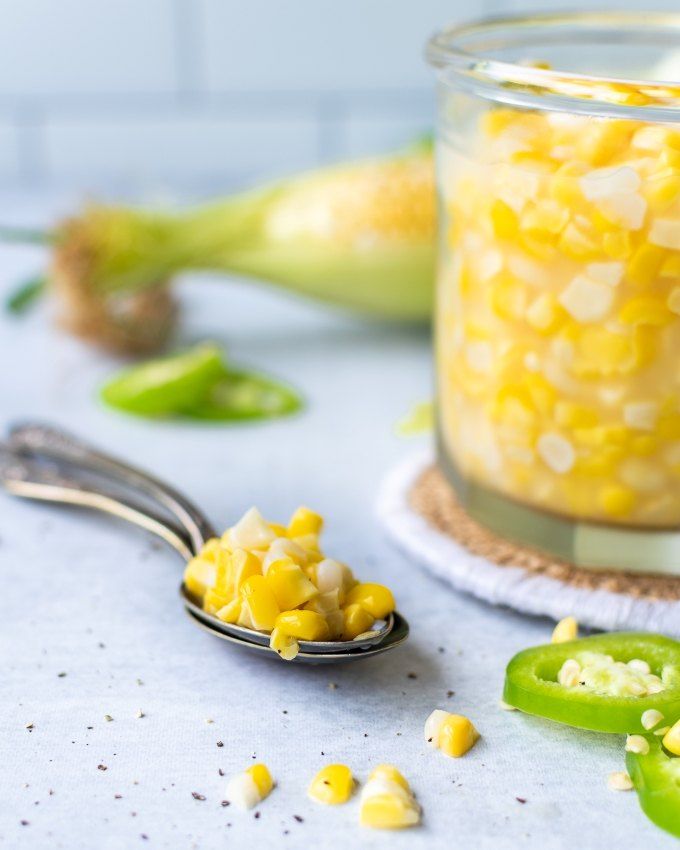 a spoon full of corn on the cob next to green peppers and banana peels