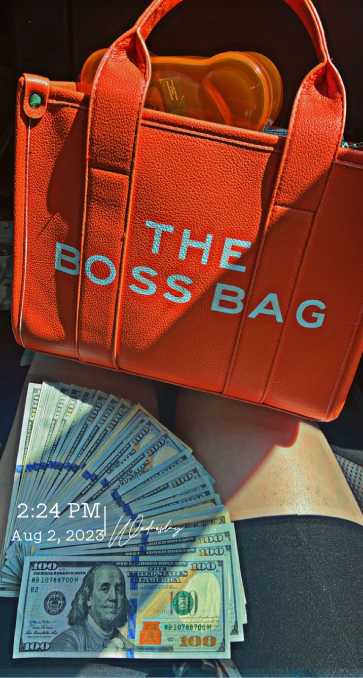 a red purse with the word the boss bag on it sitting next to some money