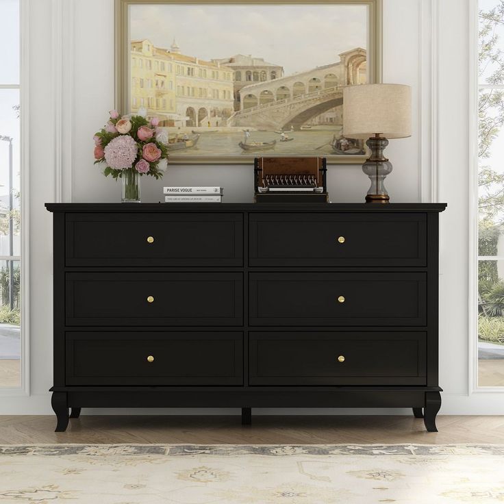 a black dresser with flowers and a painting on the wall