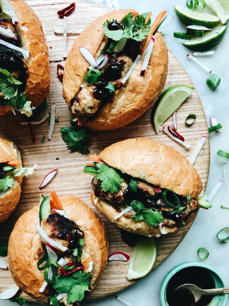 four sandwiches with meat, lettuce and onions on a wooden platter next to some dipping sauce