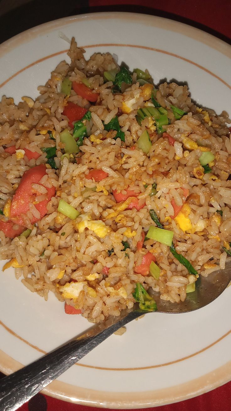 a white plate topped with rice and veggies next to a fork on a table