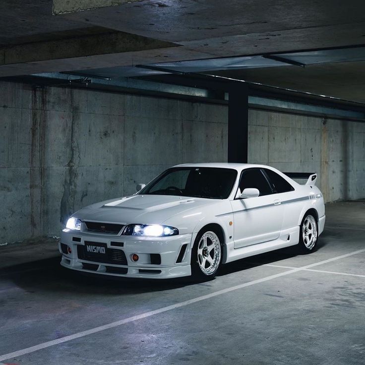 a white car is parked in an empty parking garage with concrete walls and flooring