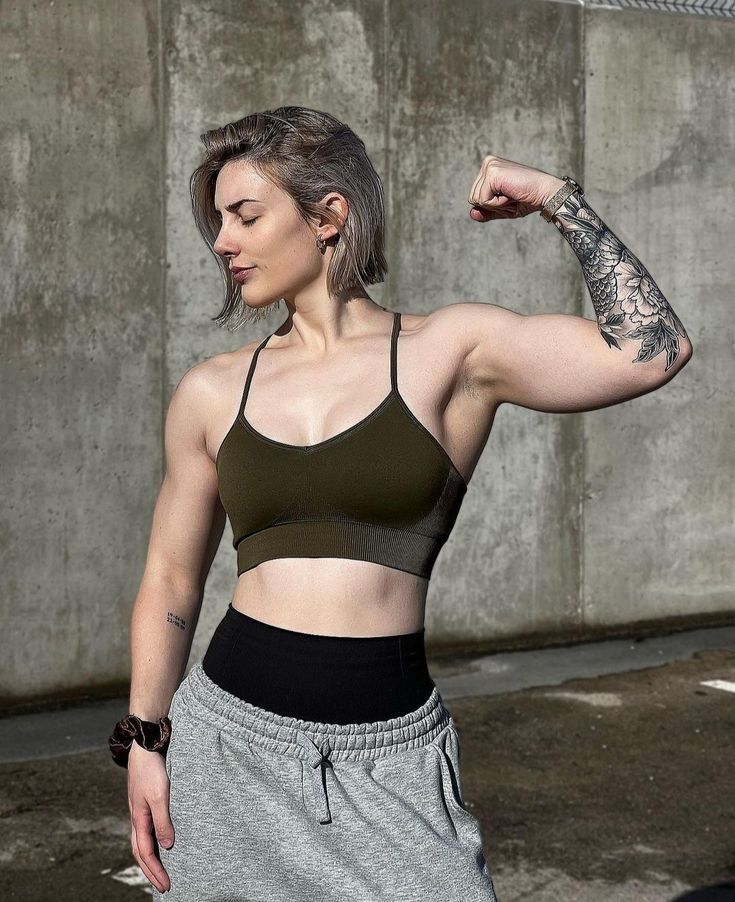 a woman with tattooed arms and arm muscles flexing while standing in front of a concrete wall