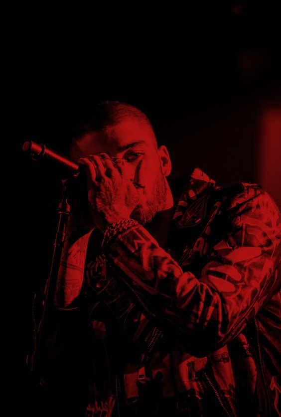 a man holding a microphone up to his mouth while standing in front of a red light