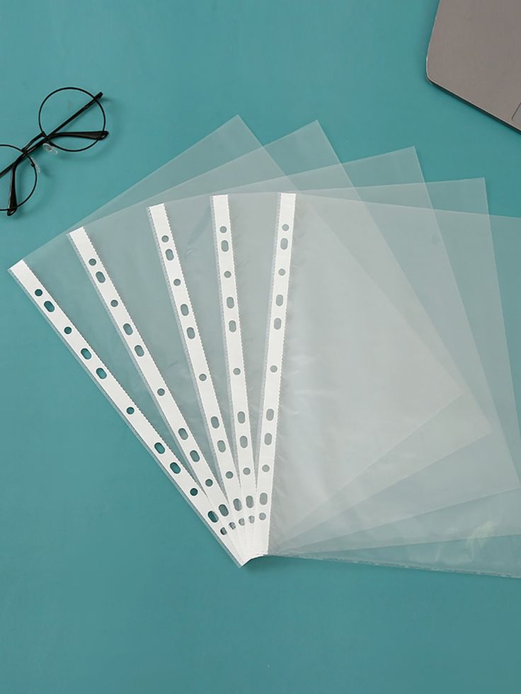 five clear plastic folders sitting on top of a blue table next to a pair of glasses