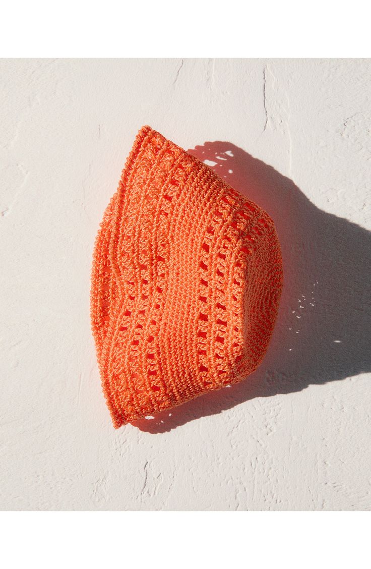 an orange knitted hat laying on top of a white wall next to a shadow