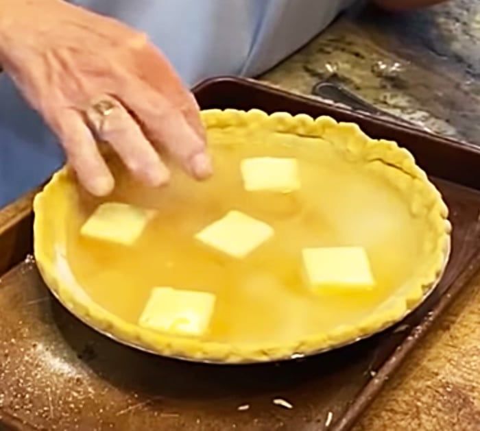 a person placing cubed cheese on top of a pie crust