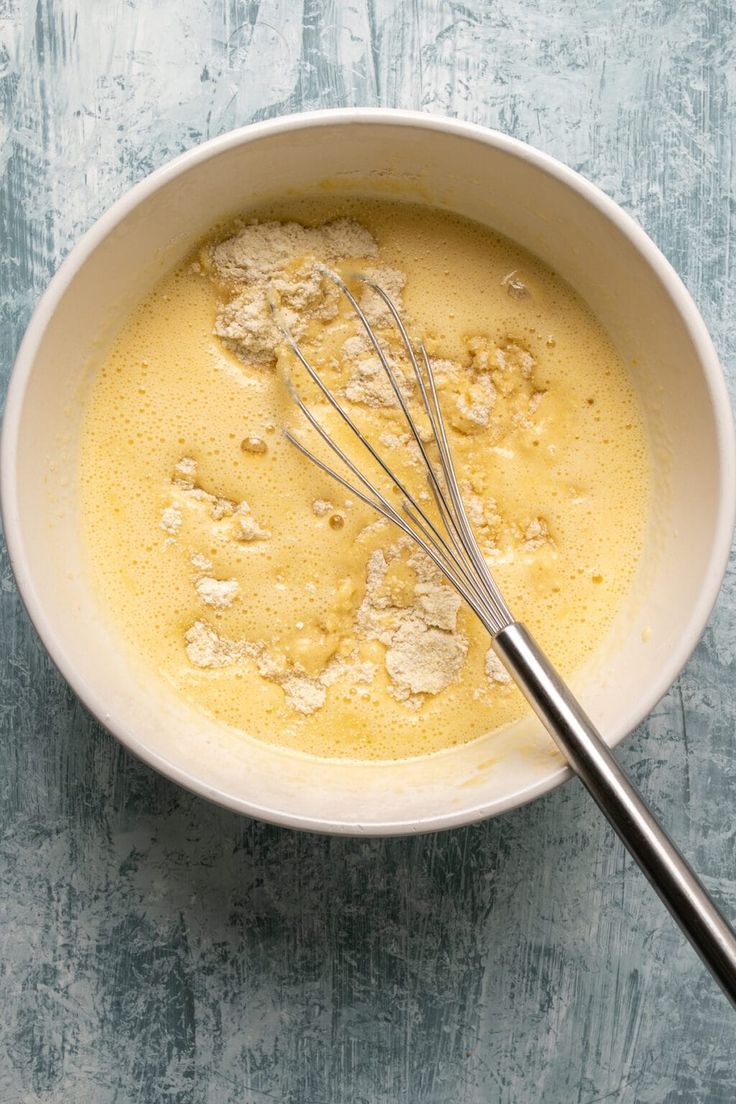 a bowl filled with batter and whisk on top of a blue tablecloth