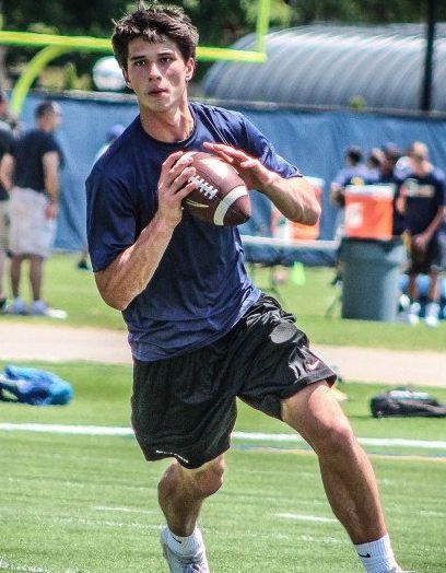 a young man holding a football on top of a green grass covered field with people in the background