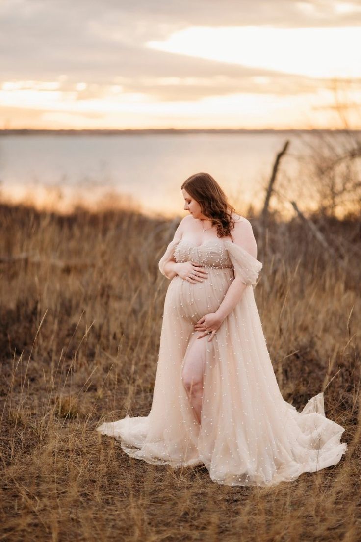 a pregnant woman is standing in the grass with her hands on her belly and wearing a flowing dress