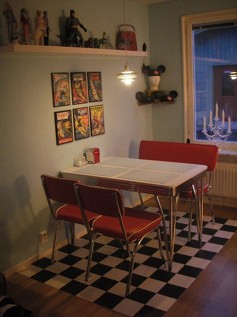 a dining room table with red chairs and pictures on the wall above it, in front of a black and white checkered floor