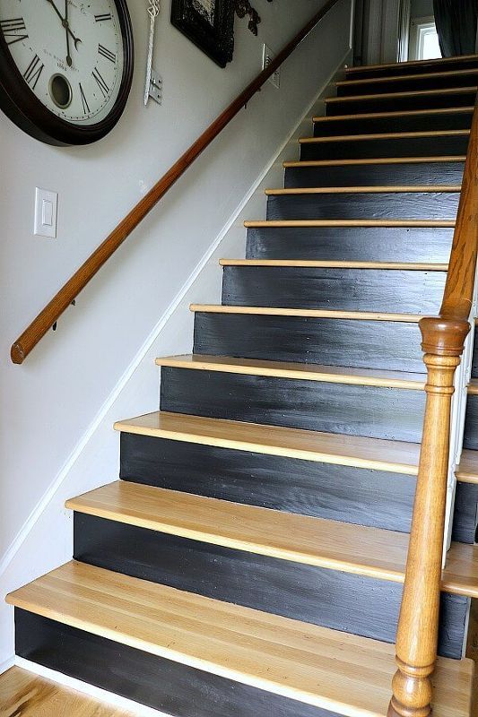 there is a clock on the wall next to some stairs and a wooden handrail