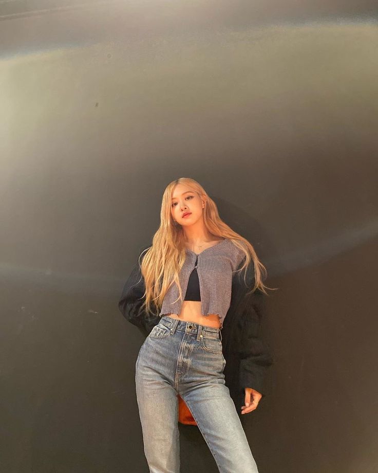 a woman standing in front of a wall wearing high waisted jeans and a crop top