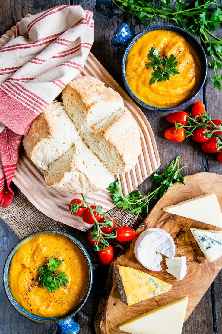 two bowls of soup, bread and cheese on a wooden table with red and white towels