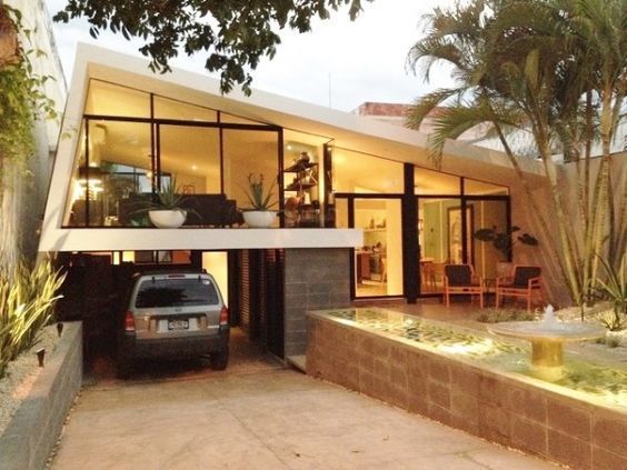 a car is parked in front of a house with large windows and plants on the outside