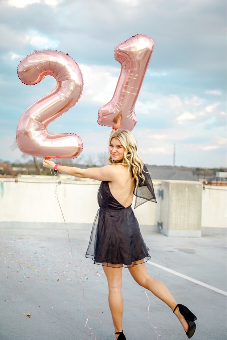 a woman in a black dress is holding some pink balloons