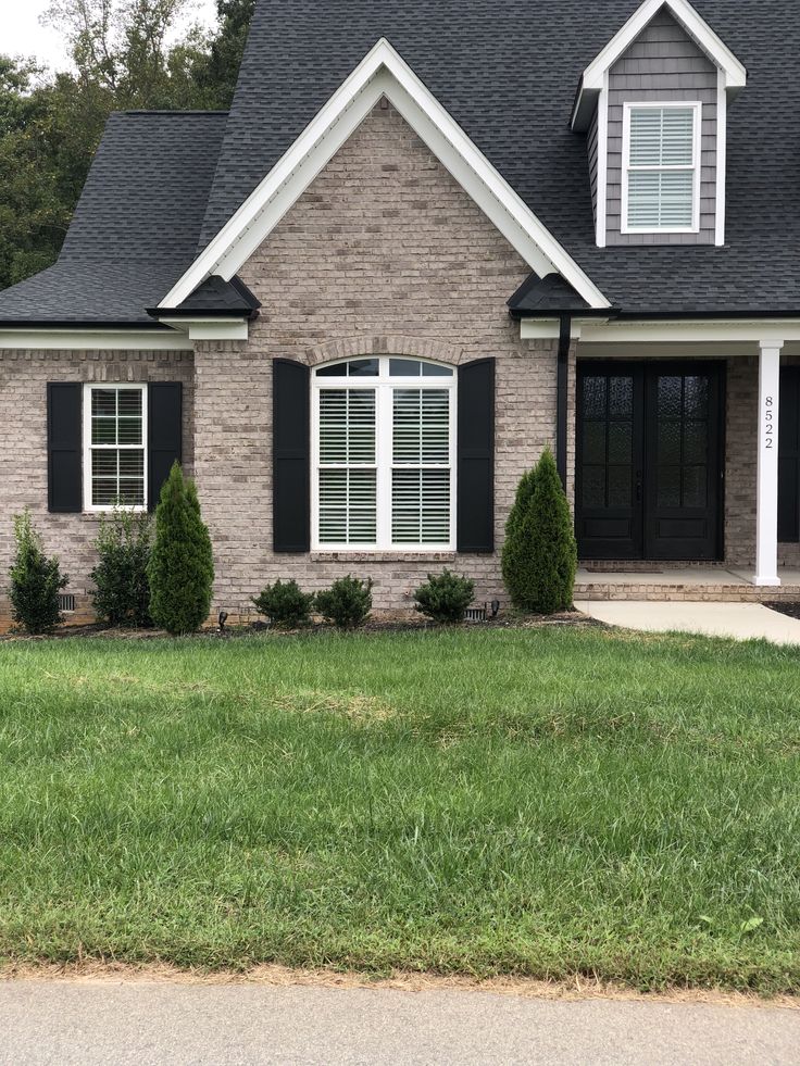 a brick house with black shutters and white trim on the front door, grass in front